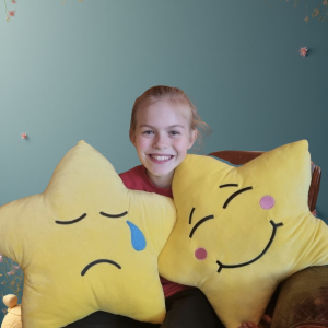 Little girls sits with two yellow star-shaped cushions with happy and sad faces on them